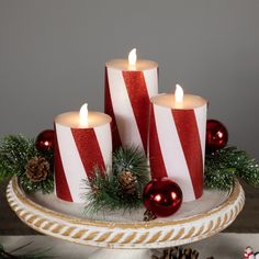 three red and white striped candles sitting on top of a platter filled with christmas decorations