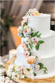 a three tiered white cake with flowers on the side and greenery around it