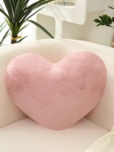 a pink heart shaped pillow sitting on top of a white couch next to a potted plant