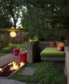 a fire pit in the middle of a yard with green furniture and pillows on it