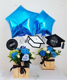 two vases filled with blue flowers and graduation hats on top of a white table