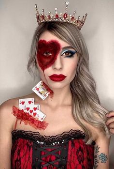 a woman with makeup on her face is wearing a crown and holding playing cards in front of her face