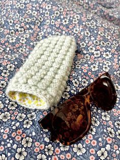 a pair of sunglasses laying on top of a flowery bed sheet with a crocheted cover