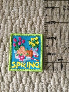 there is a small patch with flowers on it next to a ruler that says spring