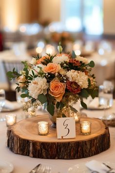 a centerpiece with candles and flowers on a wooden slice at a wedding reception table