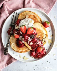 pancakes topped with strawberries and whipped cream on a white plate next to a fork