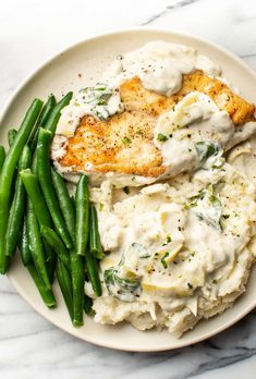 a white plate topped with green beans and chicken covered in gravy on top of mashed potatoes