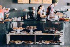 people are standing at the counter in a bakery with pastries and cakes on display