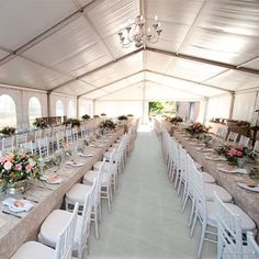 a long table set up with white chairs and flowers