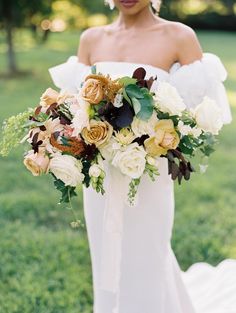 a bride holding a bouquet of flowers in her hands and wearing a wedding dress with an off the shoulder neckline