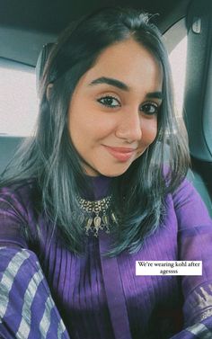 a woman sitting in the back seat of a car wearing a purple top and gold necklace