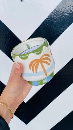 a hand holding a cup with a palm tree painted on the inside and bottom, in front of a black and white striped wall