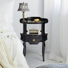 a black table with a lamp on it next to a night stand and bedding