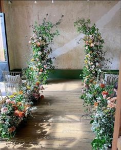 an arch made out of flowers on the side of a wooden floor in front of a wall