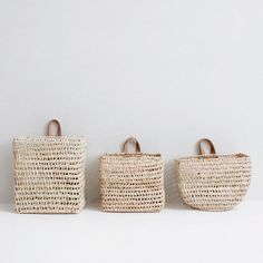 three woven bags are lined up against a white wall, one is brown and the other is beige