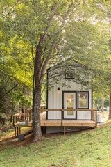 a tiny house in the woods with trees and grass on the ground, next to it is