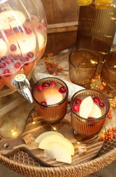 three glasses filled with liquid and fruit on a tray next to some apples, oranges and cranberries