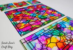 three stained glass panels with different colors and shapes in them on a white table top