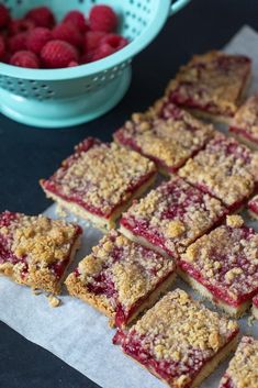 raspberry crumb bars cut into squares and placed next to a bowl of strawberries