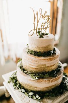 a three tiered cake with greenery and a wooden sign that says where we are