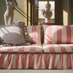 a pink and white striped couch sitting in front of a window next to a statue