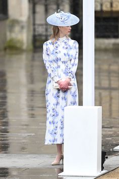 a woman in a blue hat and dress standing next to a lamp post on a rainy day