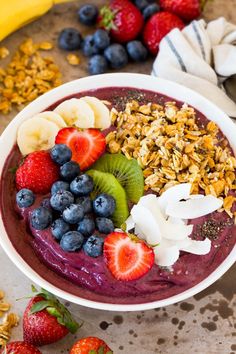 a bowl filled with fruit and granola on top of a table next to bananas