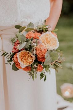 a bride holding a bouquet of orange and white flowers on her wedding day with candles in the background