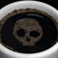 a white bowl filled with black liquid and a gold skull on the inside of it