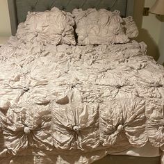 an unmade bed with white sheets and ruffled bedspread on the headboard