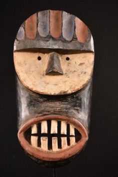 a wooden mask hanging from the side of a wall with teeth on it's face