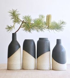 three black and white vases sitting on top of a table next to a pine branch