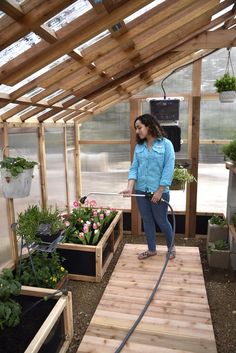 a woman watering plants in a greenhouse with a hose attached to the side of her head