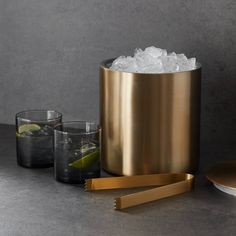 a gold ice bucket with two glasses next to it on a gray surface and another glass in the foreground