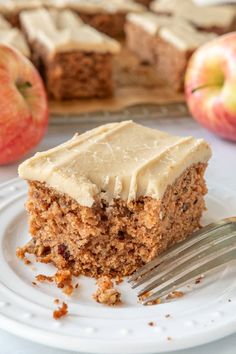 a piece of carrot cake on a plate with a fork next to it and an apple in the background