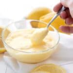 a person is dipping something into a small glass bowl with lemons in the background