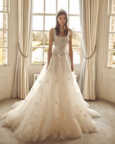 a woman standing in front of a window wearing a wedding dress with flowers on it