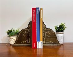 two books are sitting next to each other on a wooden table with potted plants