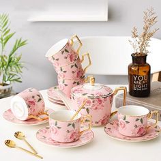 pink and gold tea set with matching saucers, cups and spoons on a white table