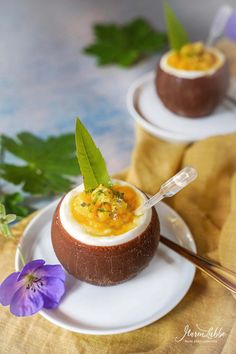 two plates with deviled eggs on them, one has a spoon in it and the other has a purple flower