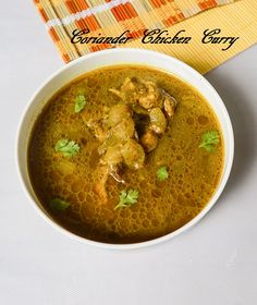 a white bowl filled with chicken curry next to a yellow napkin and orange place mat