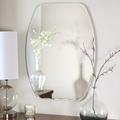 a mirror sitting on top of a wooden table next to a vase with flowers in it