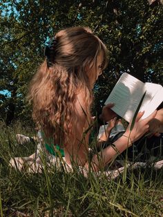 a girl reading a book in the grass under a tree with her head turned to the side