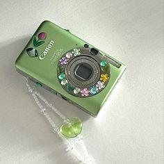 a green digital camera sitting on top of a white table next to a string of beads