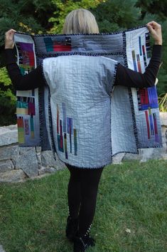 a woman is holding up a quilted blanket in the grass with trees behind her