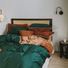 a bed with green and brown sheets in a room next to a lamp on a table