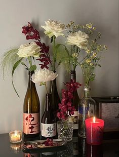 three wine bottles with flowers and candles on a table