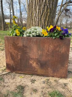 a metal planter with flowers in it sitting next to a tree and dirt ground