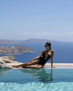 a woman sitting on the edge of a swimming pool in front of an ocean view