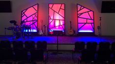 the stage is set up for an event with purple lighting and black chairs in front of it